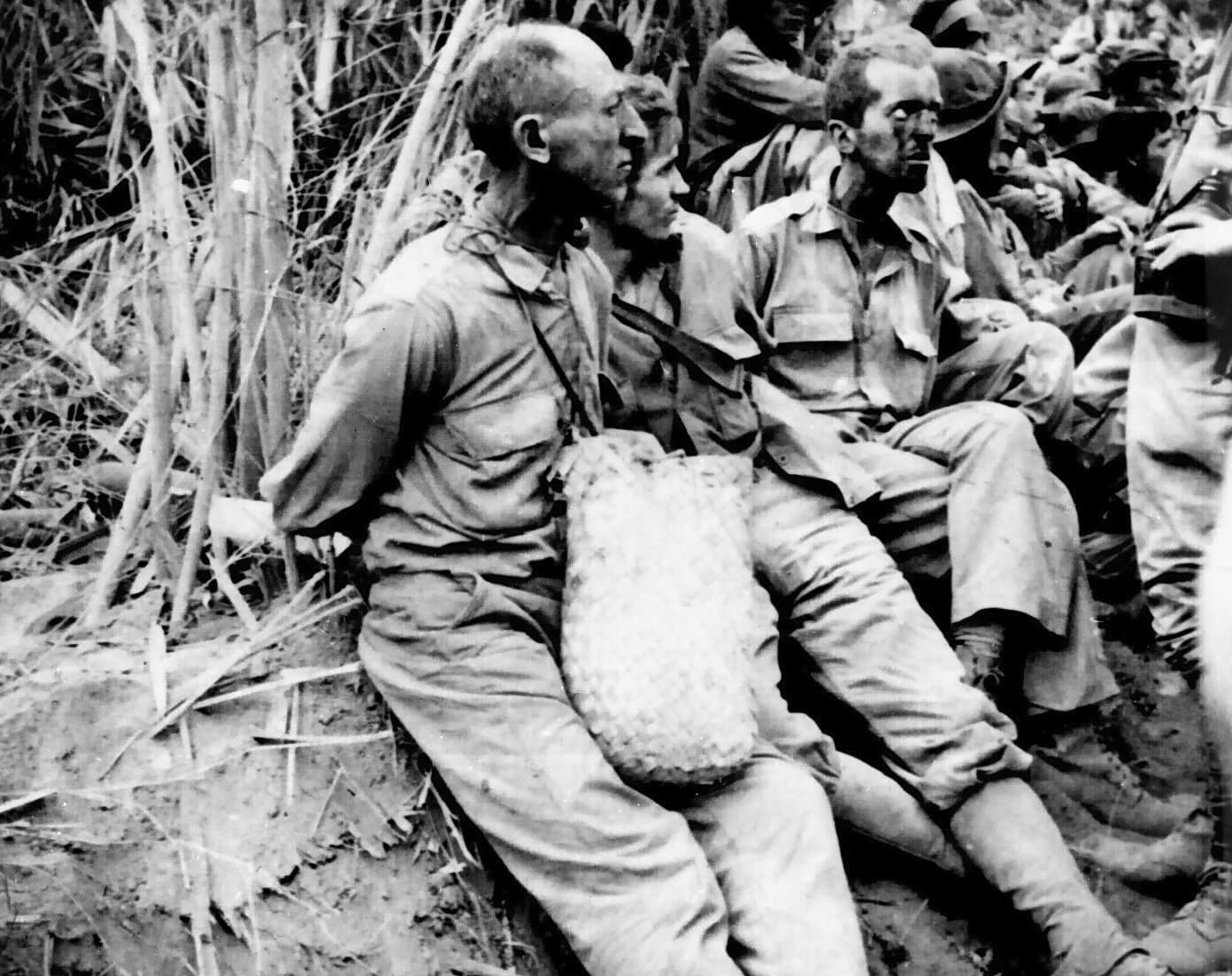 Prisoners with hands tied behind their backs rest by the roadside during the 1942 Bataan Death March