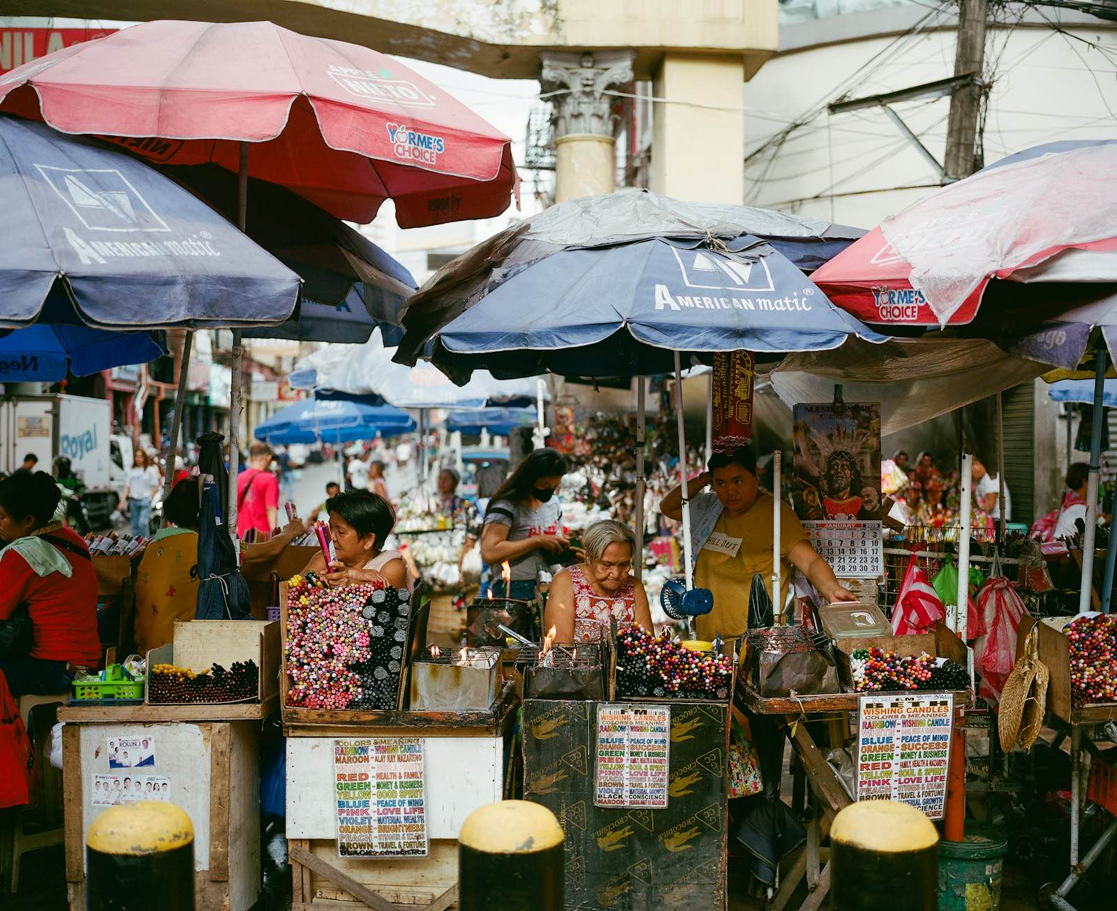Vendors sell flowers and goods under large umbrellas at a busy outdoor market in the Philippines