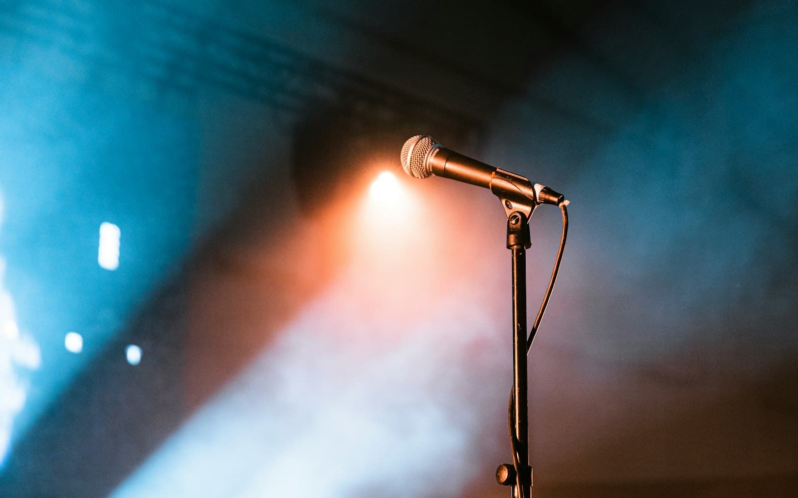 A microphone on a stand under warm stage lights and haze, waiting for the next speaker