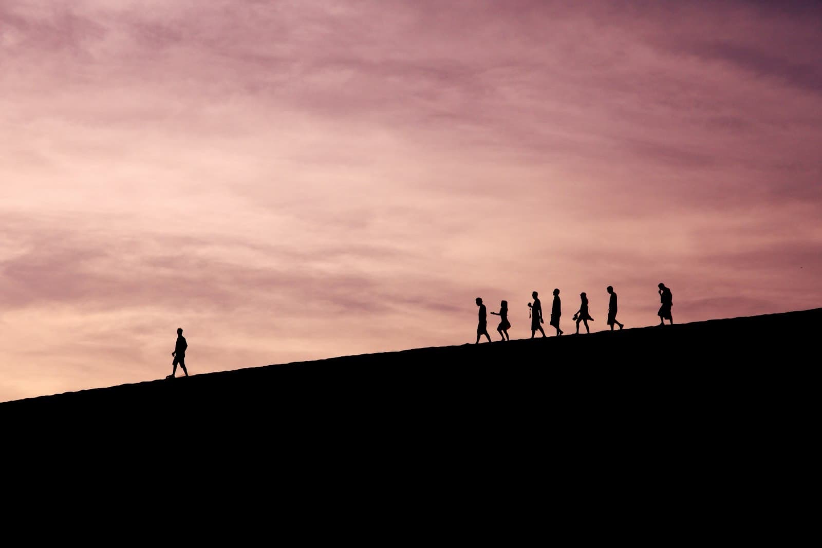 Silhouette of one person walking ahead of a group along a ridge at dusk