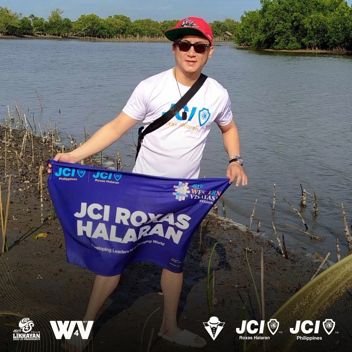 A JCI Roxas Halaran member holding the chapter banner beside young mangroves at Culajao Mangrove Ecopark
